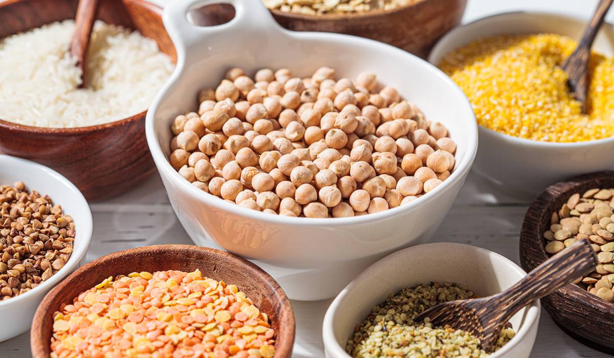 Assorted dry cereals and legumes in white and wooden bowls, white background. Vegan protein concept.